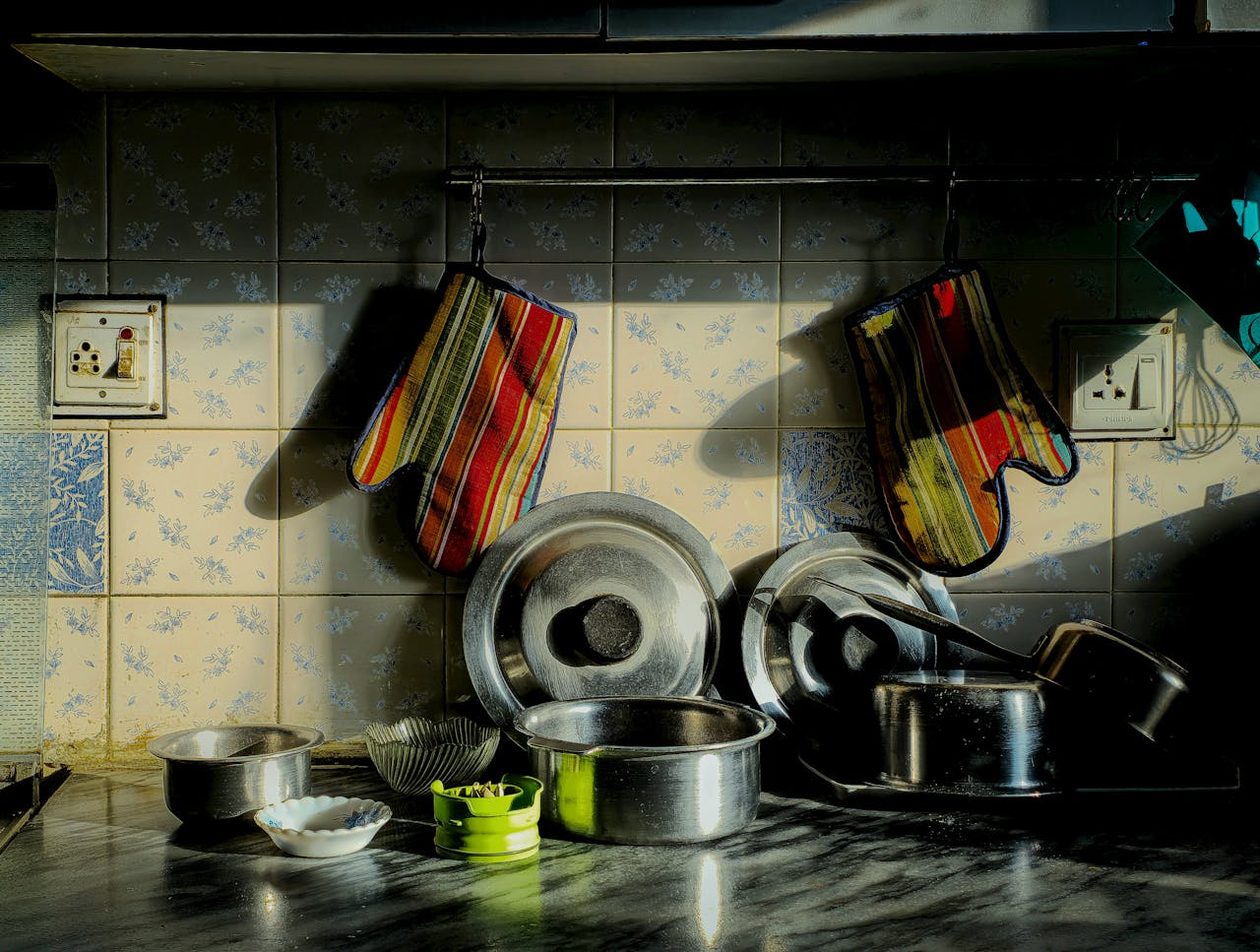 A warm kitchen setting with colorful oven mitts and stainless steel pots.