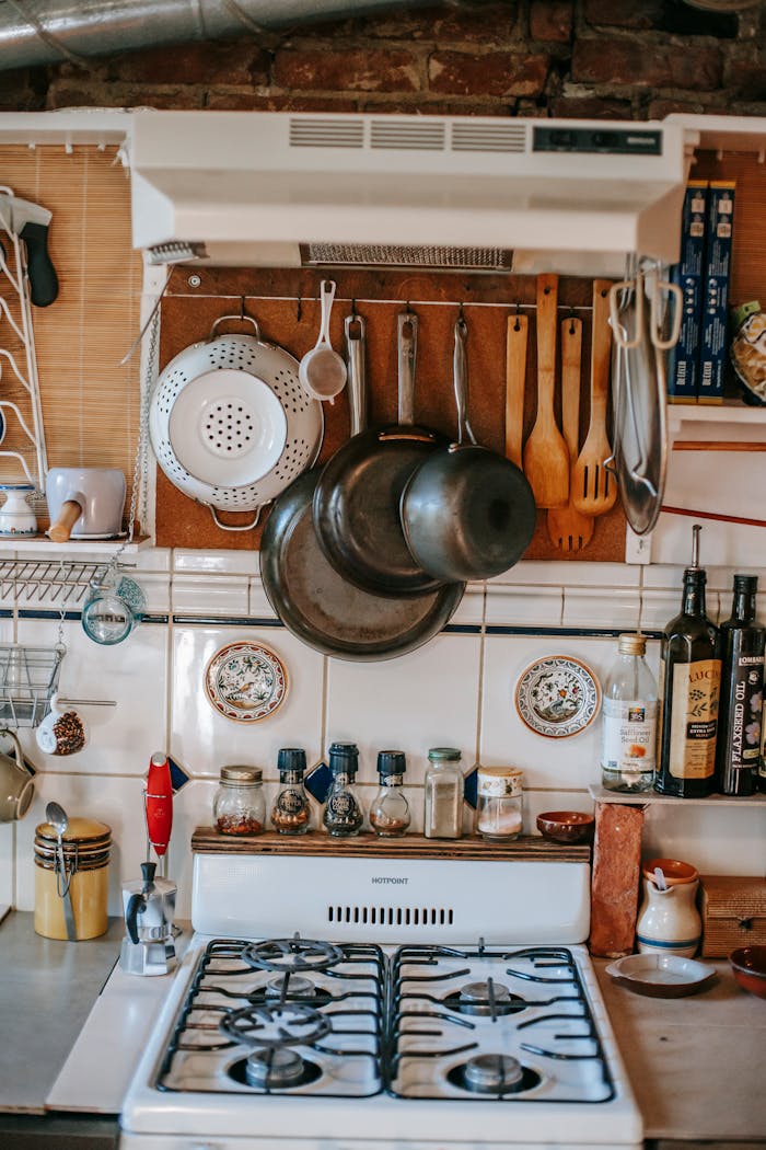 Collection of pans and culinary utensils near shelves with condiment bottles over gas stove at home