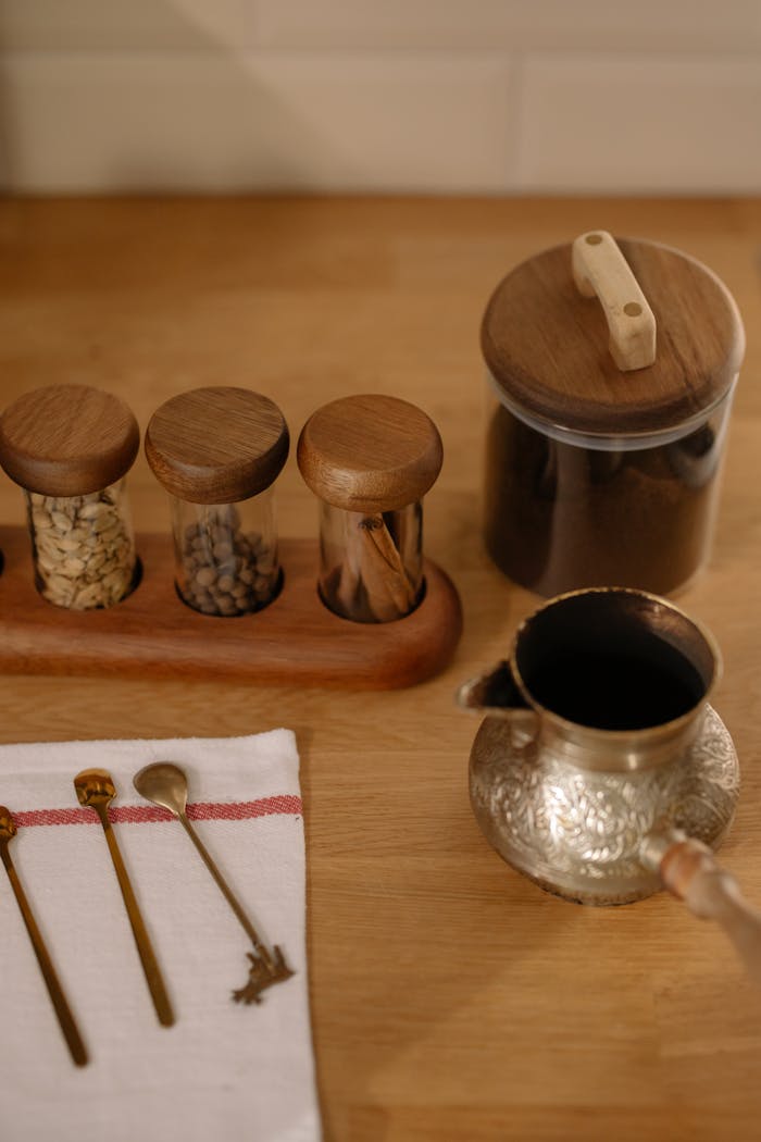 A rustic kitchen scene featuring wooden spice containers, a coffee pot, and vintage spoons on a towel.