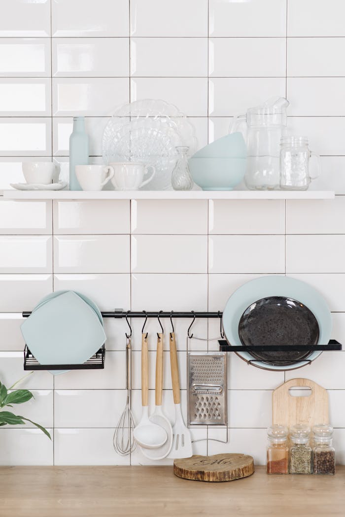 Neatly arranged kitchen items on a white tiled wall, showcasing simplicity and style.